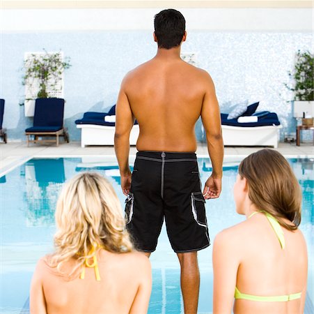 simsearch:640-03265643,k - Vue arrière d'un homme adult moyen debout devant deux jeunes femmes au bord de la piscine Photographie de stock - Premium Libres de Droits, Code: 625-00843080