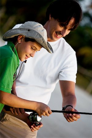 Close-up of a boy holding a fishing rod with his father Stock Photo - Premium Royalty-Free, Code: 625-00899736