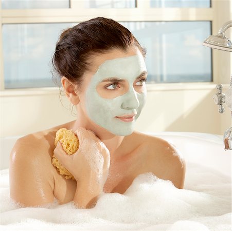 Close-up of a young woman with a facial mask holding a bath sponge Stock Photo - Premium Royalty-Free, Code: 625-00900435