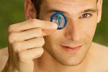 simsearch:625-01252359,k - Portrait of a young man holding a condom in front of his eye Stock Photo - Premium Royalty-Free, Code: 625-00900433