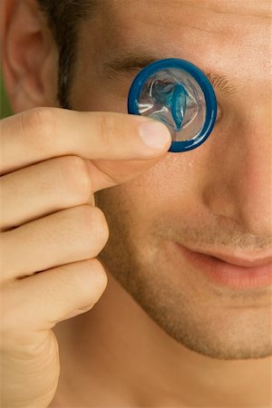 Close-up of a young man holding a condom in front of his eye Stock Photo - Premium Royalty-Free, Code: 625-00900462