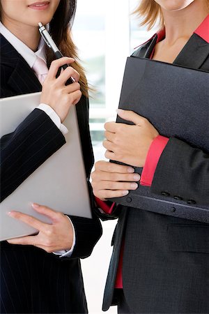 Close-up of two businesswomen holding a file and a laptop Stock Photo - Premium Royalty-Free, Code: 625-00900472