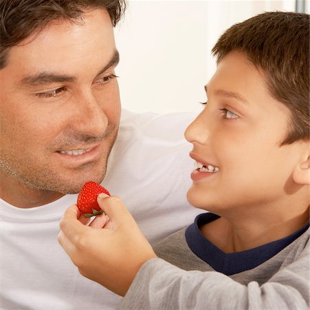 Close-up of a boy feeding his father a strawberry Stock Photo - Premium Royalty-Free, Code: 625-00900953