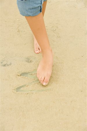 Low section view of a woman drawing in sand with her toe Stock Photo - Premium Royalty-Free, Code: 625-00902512