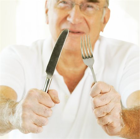 Portrait of a senior man holding a fork with a table knife Stock Photo - Premium Royalty-Free, Code: 625-00902525