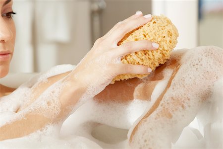 Close-up of a young woman using a bath sponge on her arm Stock Photo - Premium Royalty-Free, Code: 625-00902540
