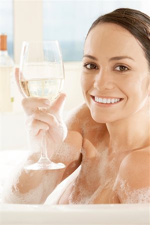 Portrait of a young woman holding a glass of white wine in the bathtub Stock Photo - Premium Royalty-Free, Code: 625-00902814