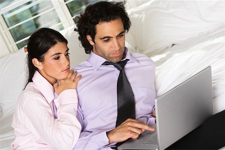 Close-up of a businessman and a businesswoman sitting on the bed using a laptop Stock Photo - Premium Royalty-Free, Code: 625-00903057