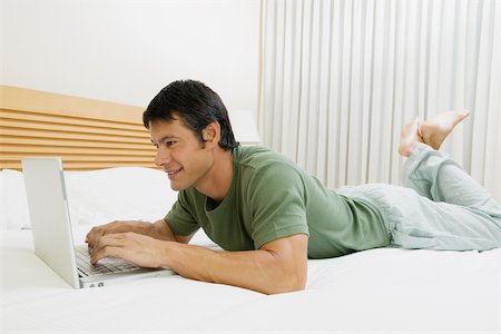 Side profile of a mid adult man lying on the bed and using a laptop Stock Photo - Premium Royalty-Free, Code: 625-01038964