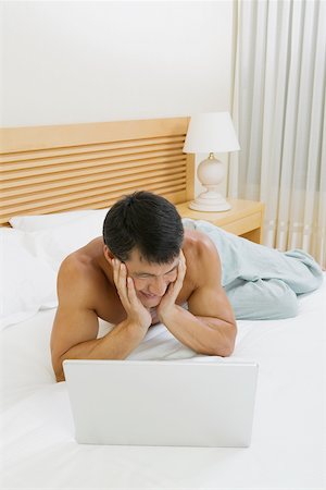 Mid adult man lying on the bed with a laptop in front of him Stock Photo - Premium Royalty-Free, Code: 625-01039004