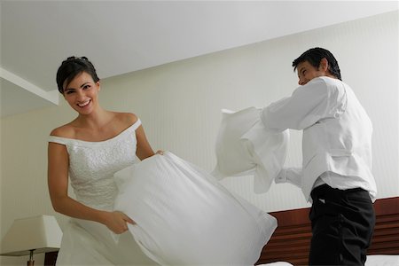 Newlywed couple having a pillow fight on the bed Stock Photo - Premium Royalty-Free, Code: 625-01039031