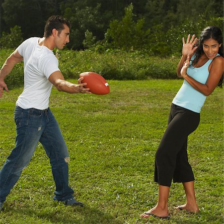 female in flip flops and jeans - Mid adult man standing holding a football in front of a young woman Stock Photo - Premium Royalty-Free, Code: 625-01039302