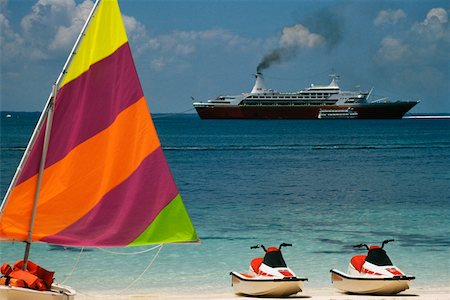 sailing beach - Side view of a boat with a colorful sail with the Starship Majestic Cruise Ship in the background, Treasure Island, Stock Photo - Premium Royalty-Free, Code: 625-01040365