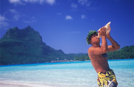 Side profile of a young man blowing a conch shell on the beach, Hawaii, USA Stock Photo - Premium Royalty-Free, Code: 625-01094799