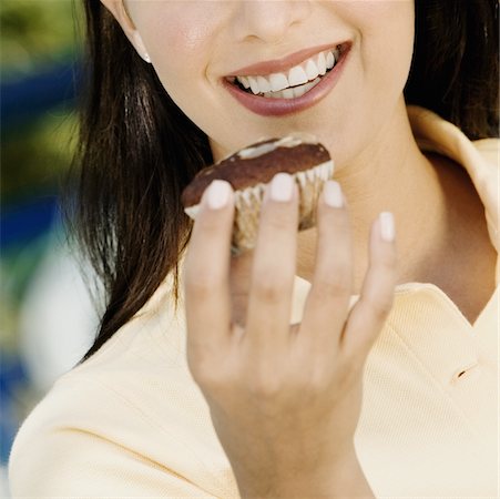 Close-up of a young woman holding a cupcake and smiling Stock Photo - Premium Royalty-Free, Code: 625-01095379