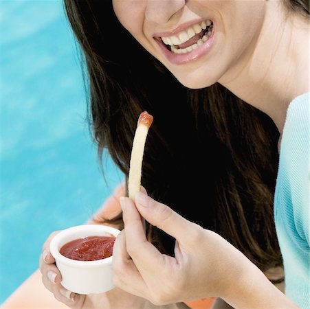 french fry smile - Close-up of a young woman holding French fries with dip and smiling Stock Photo - Premium Royalty-Free, Code: 625-01095386