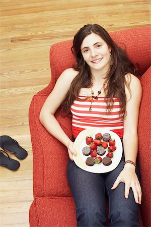 High angle view of a young woman lying on a couch and holding a plate of strawberries with chocolates Foto de stock - Sin royalties Premium, Código: 625-01096439