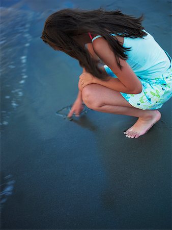 High angle view of a teenage girl drawing in the sand with her finger Stock Photo - Premium Royalty-Free, Code: 625-01097095
