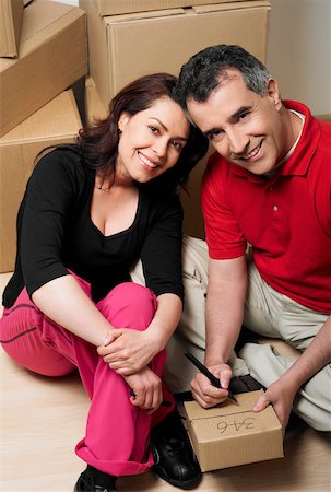 Portrait of a mid adult man writing on a cardboard box with a mid adult woman sitting beside him Stock Photo - Premium Royalty-Free, Code: 625-01097457