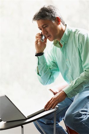 Close-up of a businessman using a laptop and talking on a mobile phone Stock Photo - Premium Royalty-Free, Code: 625-01097498