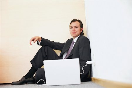 simsearch:625-01096675,k - Portrait of a businessman sitting against a wall with a laptop beside him Stock Photo - Premium Royalty-Free, Code: 625-01092819