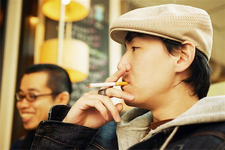 Profil de côté d'un homme adult moyen fumant une cigarette et un jeune homme souriant à côté de lui Photographie de stock - Premium Libres de Droits, Code: 625-01093029