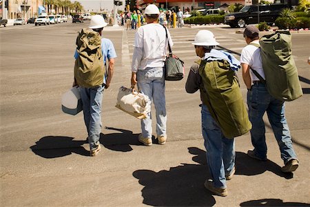 Rear view of four men crossing a road with bags Stock Photo - Premium Royalty-Free, Code: 625-01093358