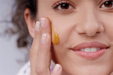 Portrait of a young woman applying honey on her cheek Stock Photo - Premium Royalty-Free, Code: 625-01093390