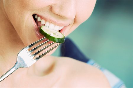 Close-up of a young woman eating a slice of cucumber with a fork Stock Photo - Premium Royalty-Free, Code: 625-01093562