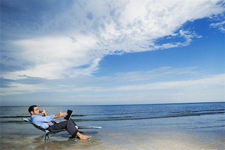 Side profile of a young man sitting on the beach with a laptop Stock Photo - Premium Royalty-Free, Code: 625-01093961