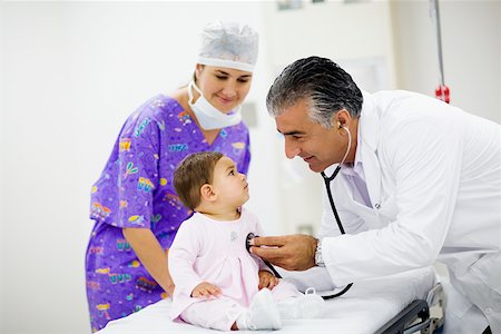 doctor checking full body - Side profile of a male doctor examining a baby girl with a stethoscope and a female doctor standing near them Stock Photo - Premium Royalty-Free, Code: 625-01250345