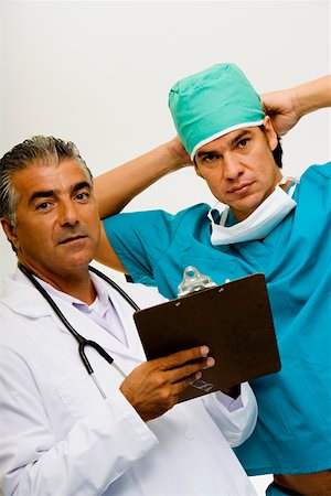 pictures of a man standing on a gap - Portrait of a male doctor holding a clipboard with a male surgeon tying his surgical cap beside him Stock Photo - Premium Royalty-Free, Code: 625-01250585