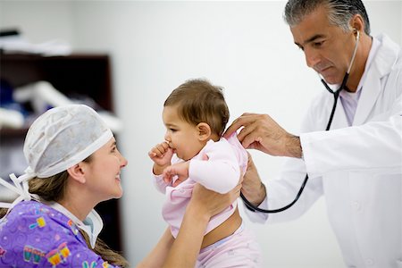 Side profile of a female doctor playing with a baby girl and a male doctor examining her Stock Photo - Premium Royalty-Free, Code: 625-01250705