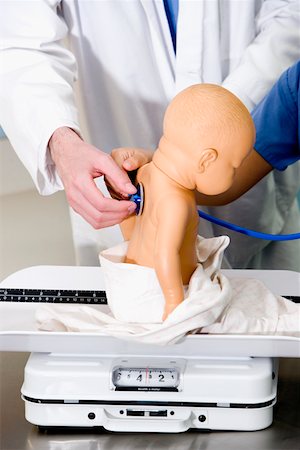 Close-up of a doll on a weighing scale being examined by a doctor with a stethoscope Stock Photo - Premium Royalty-Free, Code: 625-01250903