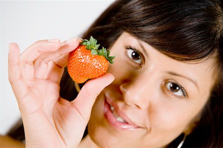 simsearch:625-00838036,k - Portrait d'une jeune femme tenant une fraise et souriant Photographie de stock - Premium Libres de Droits, Code: 625-01252140