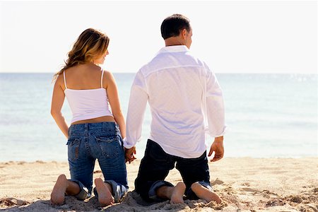 picture of woman kneeling down from behind - Rear view of a mid adult man and a young woman kneeling with holding hands on the beach Stock Photo - Premium Royalty-Free, Code: 625-01252527