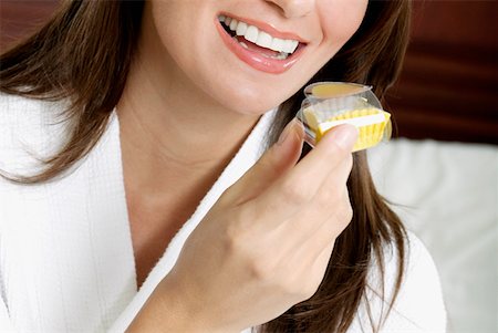 Close-up of a young woman holding a cupcake and smiling Stock Photo - Premium Royalty-Free, Code: 625-01264315