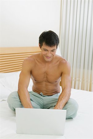 Mid adult man sitting on the bed and using a laptop Stock Photo - Premium Royalty-Free, Code: 625-01264405