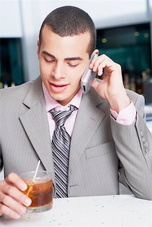 Close-up of a businessman holding a cocktail and talking on a mobile phone in a bar Stock Photo - Premium Royalty-Free, Code: 625-01264535