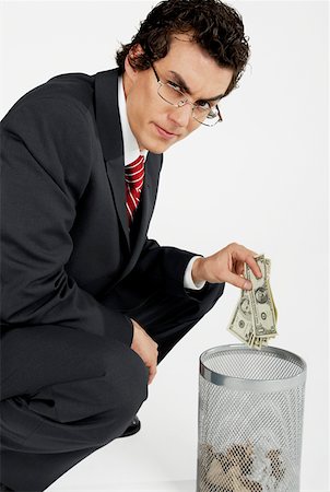 Portrait of a businessman throwing paper currency into a wastepaper basket Stock Photo - Premium Royalty-Free, Code: 625-01264774