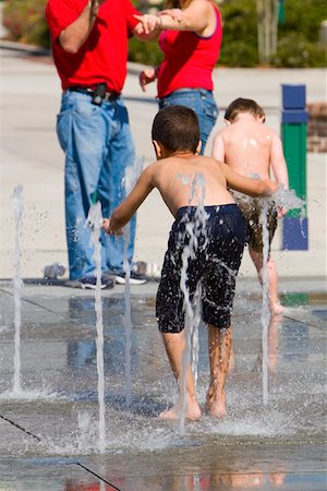 Rear view of two boys taking a bath on a fountain with a man and a woman standing in the background Stock Photo - Premium Royalty-Free, Code: 625-01265017