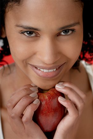 Portrait of a young woman holding an apple under her chin Stock Photo - Premium Royalty-Free, Code: 625-01261515