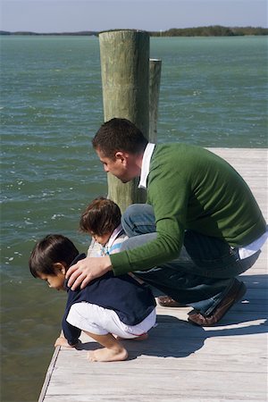 High angle view of a mid adult man with his son and daughter crouching on a pier and looking into the water Stock Photo - Premium Royalty-Free, Code: 625-01261706