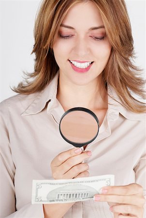 Close-up of a businesswoman examining a dollar bill with a magnifying glass and smiling Stock Photo - Premium Royalty-Free, Code: 625-01261753