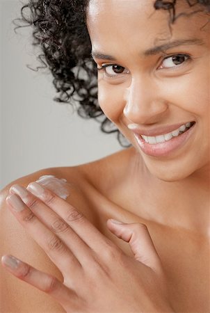 photography of body lotion and african women - Portrait d'une jeune femme, appliquer la crème hydratante sur son épaule et souriant Photographie de stock - Premium Libres de Droits, Code: 625-01263160