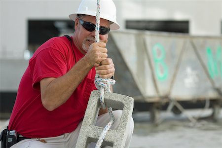 Male construction worker tightening a rope on a concrete block Stock Photo - Premium Royalty-Free, Code: 625-01745776