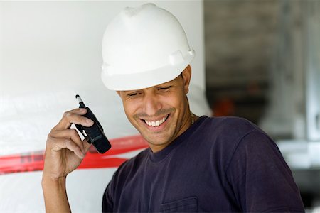 Close-up of a male construction worker talking on a walkie-talkie and smiling Stock Photo - Premium Royalty-Free, Code: 625-01745844