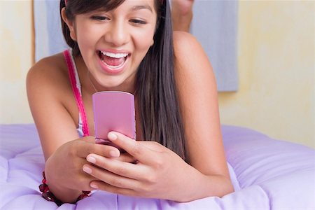 Gros plan d'une adolescente se trouvant sur le lit et les SMS sur un téléphone mobile Photographie de stock - Premium Libres de Droits, Code: 625-01746447