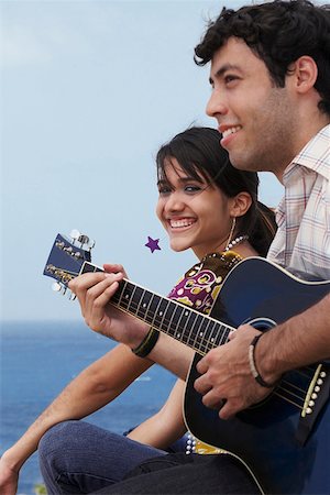 Young man sitting with a young woman and playing a guitar Stock Photo - Premium Royalty-Free, Code: 625-01746882