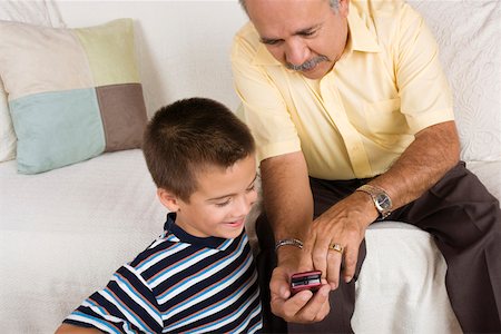 High angle view of a senior man showing a mobile phone to his grandson Stock Photo - Premium Royalty-Free, Code: 625-01746996